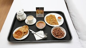 A tray with a teapot, cups, a bowl of soup, a plate of flatbread, a bowl of beans, and a packet of late-night hunger pangs snack. - OYO 23515 Shagun Hotel (Ramnagar)