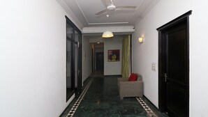 A hallway with a ceiling fan, a patterned floor, a sofa with a red cushion, and a door. - OYO Flagship 24448 Moon Light Guest House (Lucknow)