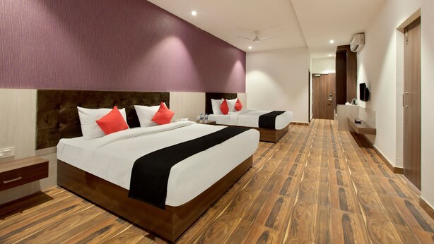 A hotel room with two beds, a wooden floor, a purple accent wall, and a ceiling fan. - Capital O 30351 S B Excellency (Jodhpur)
