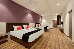 A hotel room with two beds, a wooden floor, a purple accent wall, and a ceiling fan. - Capital O 30351 S B Excellency (Jodhpur)