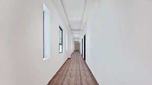 A long, narrow hallway with white walls and wooden flooring, leading to a door at the end. - Capital O 30351 S B Excellency (Jodhpur)