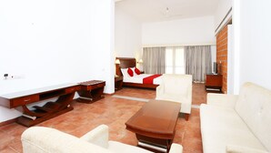 A spacious hotel room with a large bed, a sitting area with a sofa and armchairs, a wooden coffee table, and a modern desk. - Capital O 29855 Island Inn (Kanayannur)