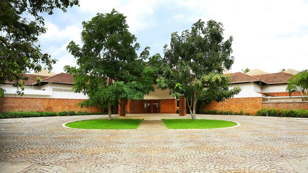 A courtyard with a cobblestone pathway leading to a building with a tiled roof. - Capital O 29855 Island Inn (Kanayannur)