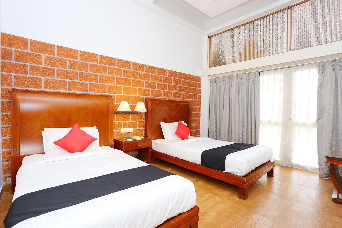 A hotel room with two beds, a brick wall, a wooden headboard, a nightstand with lamps, and a large window with curtains.