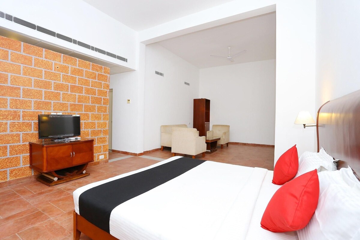 A hotel room with a bed, a television on a wooden cabinet, a seating area with two chairs, and a wardrobe.