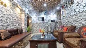 A modern living room with a stone-patterned wall, a glass-top coffee table, and two sofas with patterned upholstery.