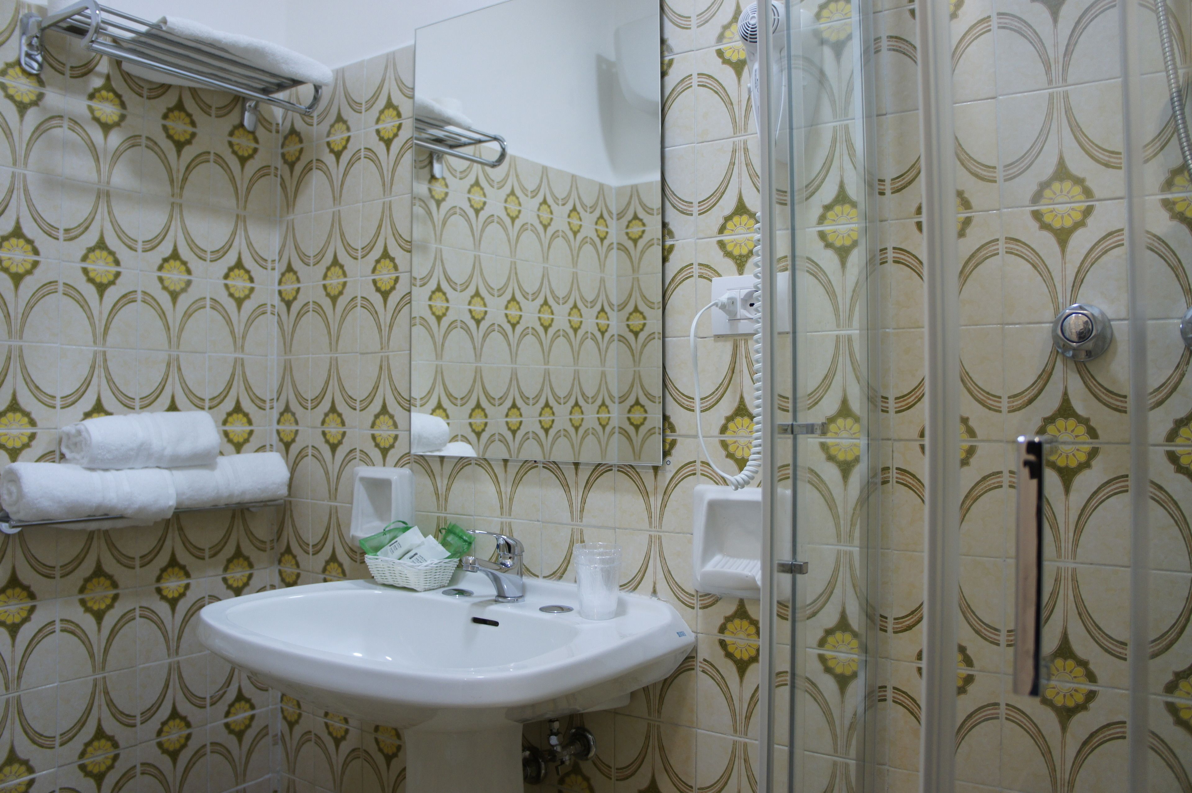 Un bagno con piastrelle decorate, un lavandino, un portascopino e una doccia.