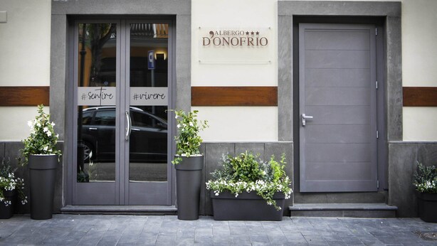 A building facade with two doors, one with glass panels and the other solid. There are potted plants in front of each door. A sign above the doors reads "Albergo Donofrio." - Albergo D'Onofrio (Telese)