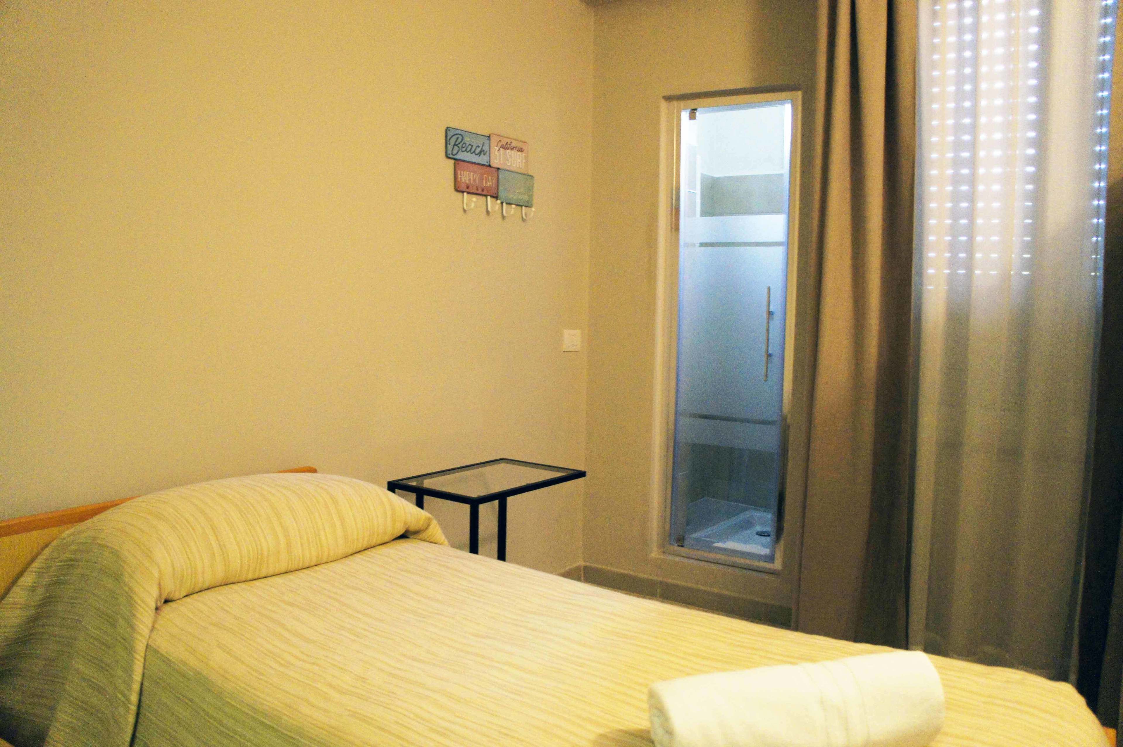 Una habitación de hotel con una cama, una mesita pequeña, una ventana con cortinas y un cartel en la pared.