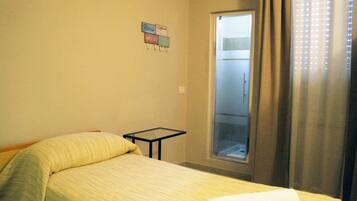 Una habitación de hotel con una cama, una mesita pequeña, una ventana con cortinas y un cartel en la pared.