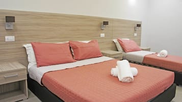 Habitació d'hotel amb dos llits, cada un amb una colcha vermella i coixins blancs. Hi ha taules de nit amb làmpades i un llum penjant a la paret.