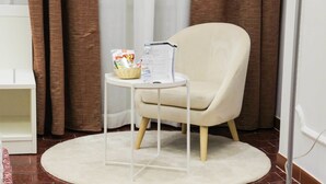 A room with a beige armchair, a small white table with a basket and a water bottle, and a white rug on a tiled floor. - Albergo D'Onofrio (Telese)