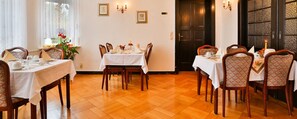 Comedor con piso de madera, manteles blancos y sillas estampadas.
