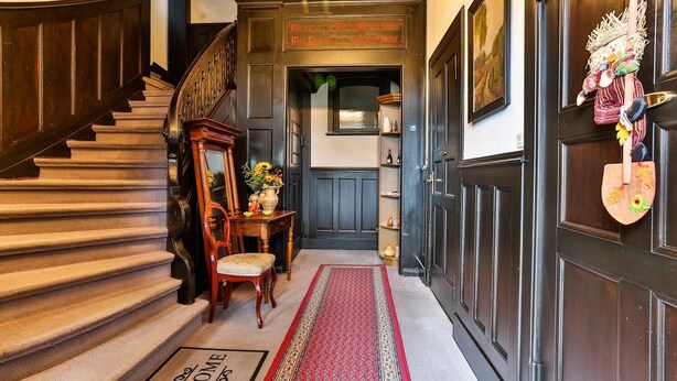 Una imponente escalera conduce a una puerta de madera oscura con felpudo.
