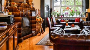 Un salón tradicional con sofás de cuero, chimenea, muebles de madera y vistas amplias por ventanas grandes.