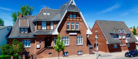 A large, two-story brick house with a steeply pitched roof, multiple windows, and a small front porch.