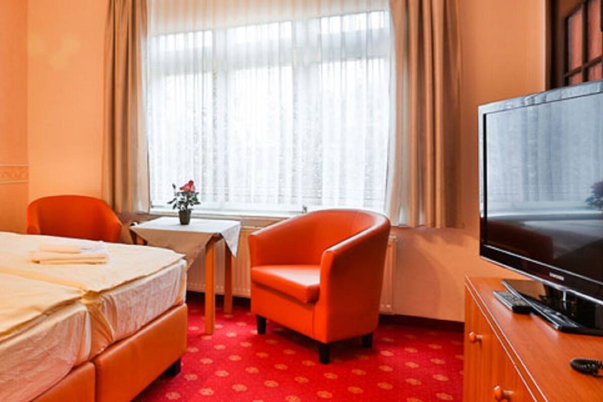 Hotellihuone, jossa on sänky, kaksi tuolia, televisio ja taulu seinällä.