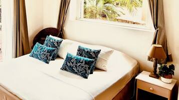 A neatly made bed with blue patterned pillows, a bedside lamp, and a window with a view of greenery.