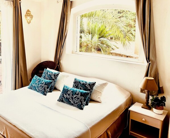A neatly made bed with blue patterned pillows, a bedside lamp, and a window with a view of greenery. - Le Mas d'Olivier (Plan-de-la-Tour)
