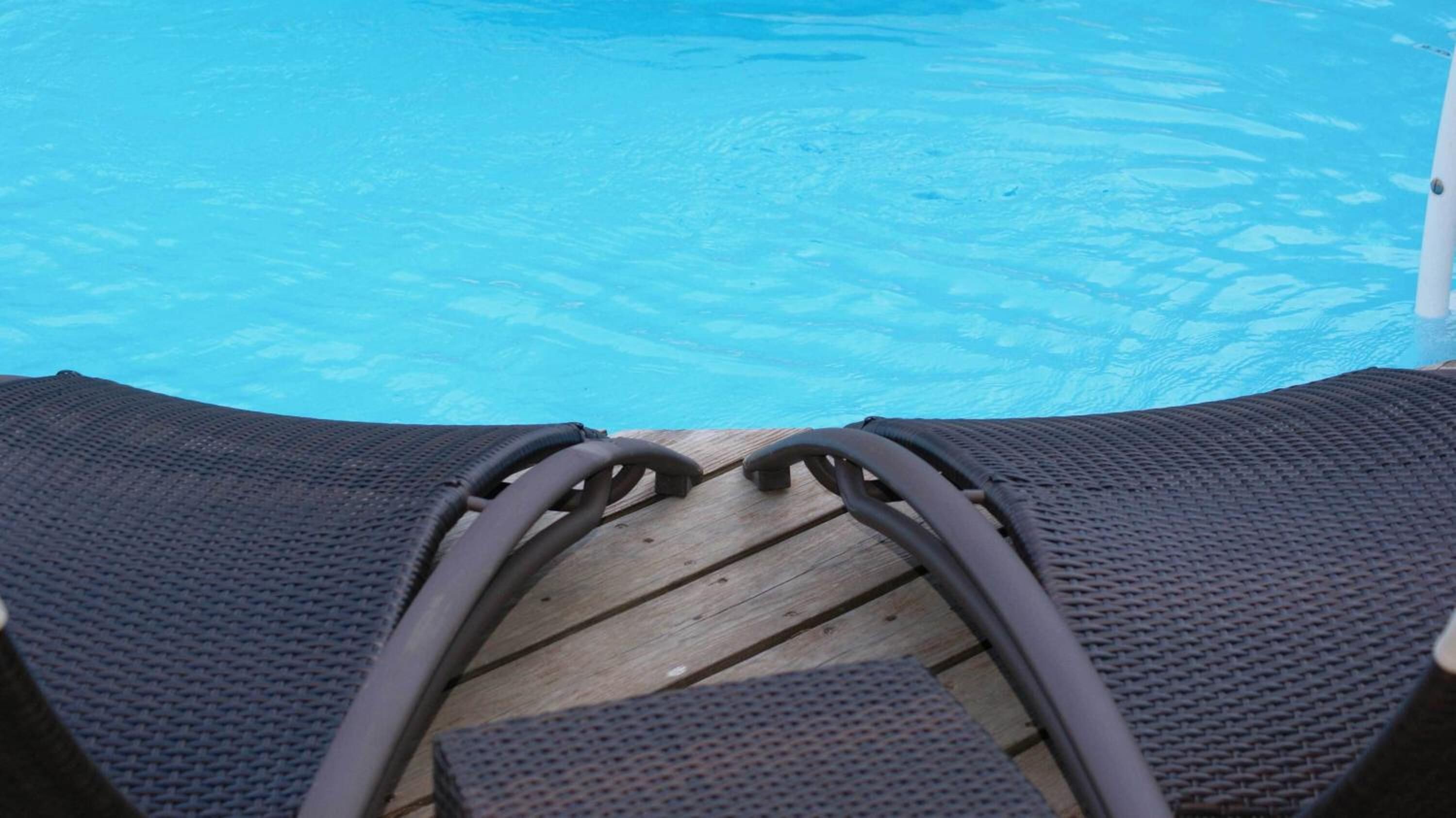 A poolside view with lounge chairs and a wooden deck.