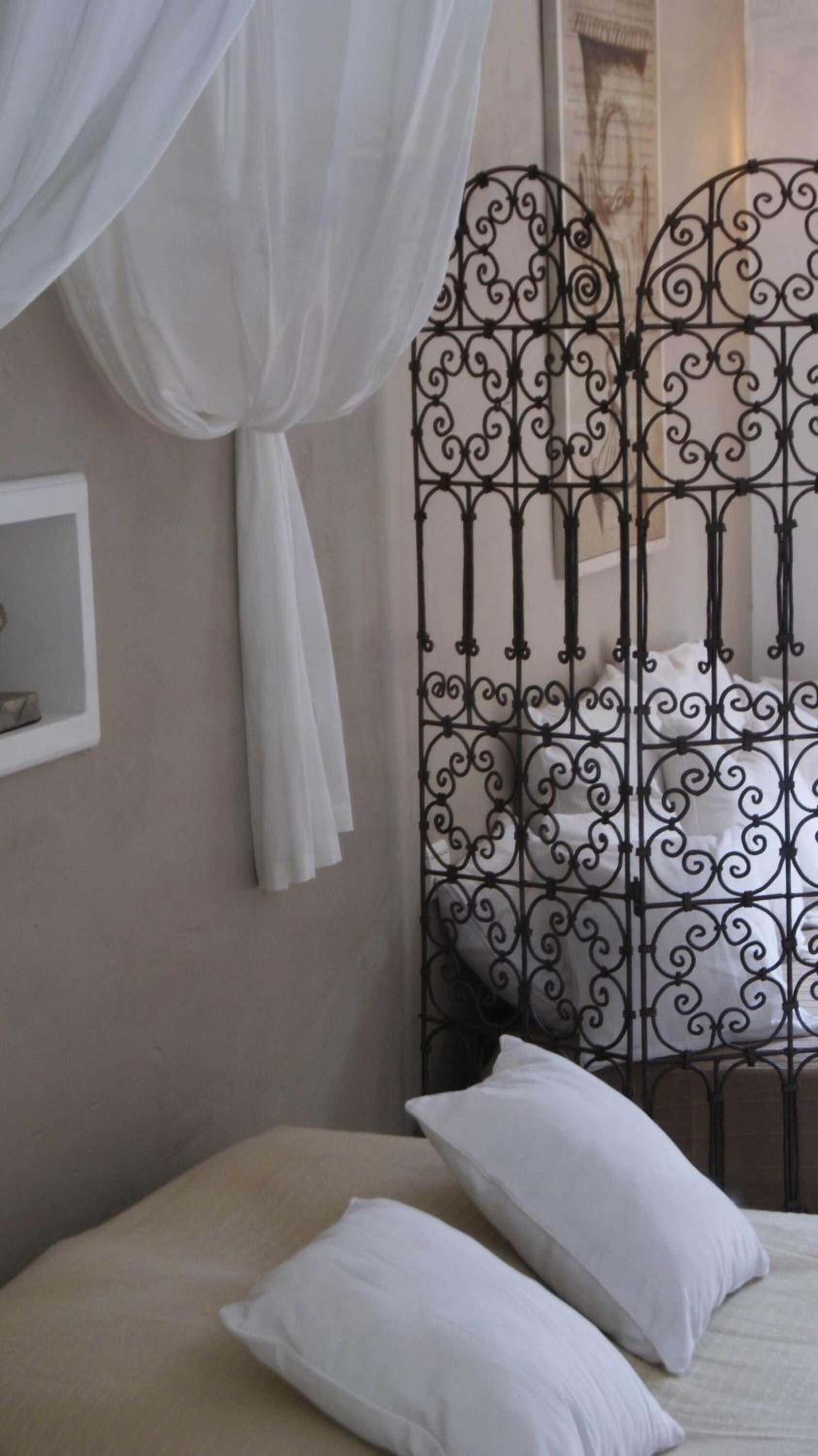 Une chambre à coucher avec un lit, des oreillers blancs, un ciel de lit blanc et une cloison décorative en métal.
