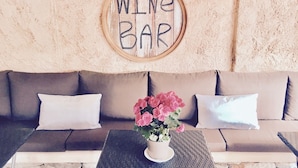 Een knus interieur met een beige bank, een tafeltje met een bloempot en een houten bordje met de tekst 'WINE BAR'.