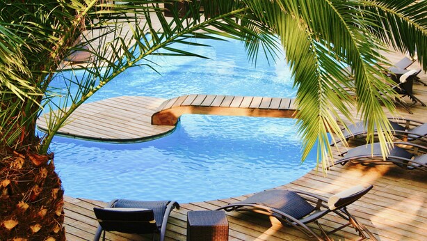 Een zwembad met een houten terras en ligbedden.