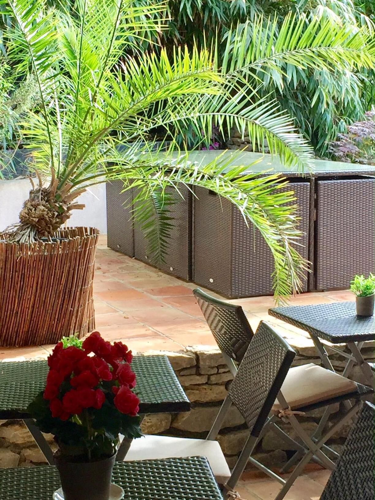An outdoor patio area with wicker furniture, a stone wall, and a variety of plants including a palm tree.
