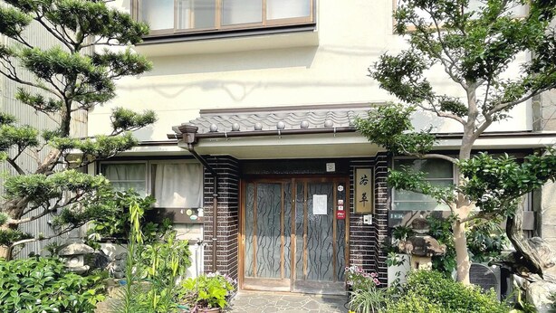 A traditional Japanese-style building with a tiled entrance, surrounded by various potted plants and trees. - Business Ryokan Wakakusa (Tsu)