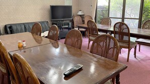 A dining area with a wooden table and chairs, a television, and a sofa. - Business Ryokan Wakakusa (Tsu)