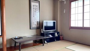 A traditional Japanese room with tatami flooring, a television on a low stand, a framed calligraphy piece on the wall, and a large window with a view. - Business Ryokan Wakakusa (Tsu)