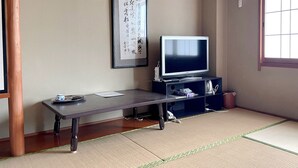 A traditional Japanese room with tatami flooring, a television on a low stand, and a framed calligraphy piece on the wall. - Business Ryokan Wakakusa (Tsu)