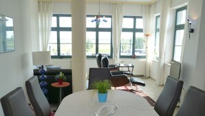 A dining area with a round table, chairs, a potted plant, and a view through large windows. - Wohnung Residenz am Wasser (Karlshagen)