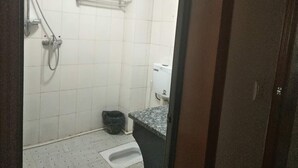 Un baño pequeño y sencillo, con ducha, inodoro y un cubo de basura.
