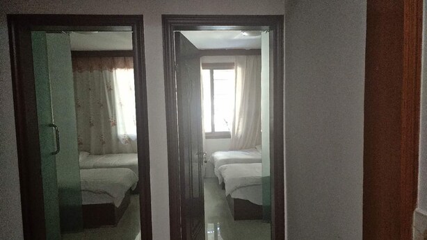 Un pasillo con dos puertas que dan a una habitación con dos camas y una ventana con cortinas.