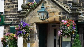 A stone building with a green door and hanging flower baskets. - Busfeild Arms (Keighley)