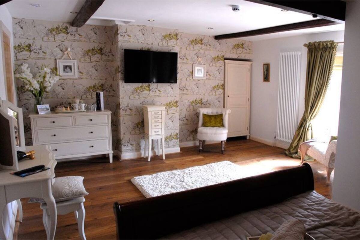 Quarto com cama, cómoda, cadeira, televisão e janela com cortinas.
