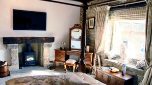 A rustic bedroom with a stone fireplace, wooden furniture, and a large window with curtains. - Busfeild Arms (Keighley)