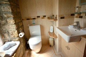 Un baño con pared de piedra, inodoro, lavamanos y espejo.