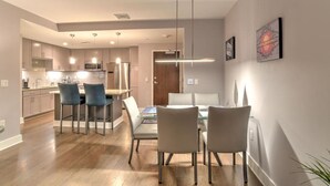 Una cucina moderna con elettrodomestici in acciaio inossidabile, un'area pranzo con tavolo in vetro e un corridoio decorato con opere d'arte.