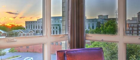 A room with a large window overlooking a parking lot and buildings, with a purple chair in the foreground.