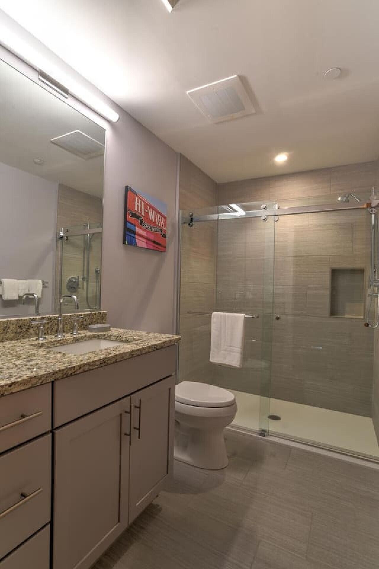 A modern bathroom with a glass shower enclosure, a marble countertop, and a toilet.