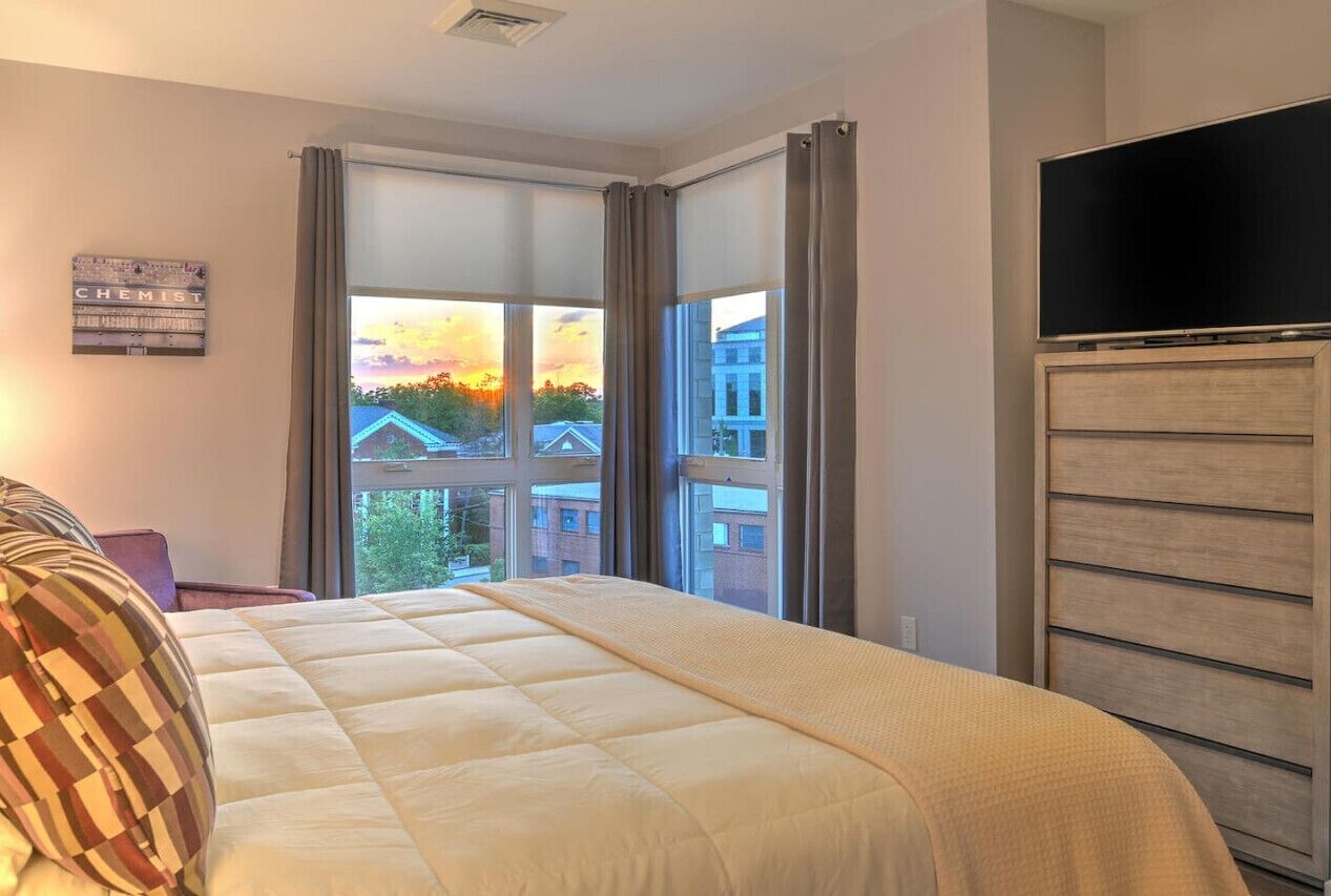 Un dormitorio con una cama grande, televisión y ventana con vista a la ciudad.