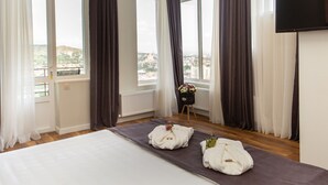 Un cuarto de hotel con una cama grande, vistas de la ciudad y una mesita con un florero.