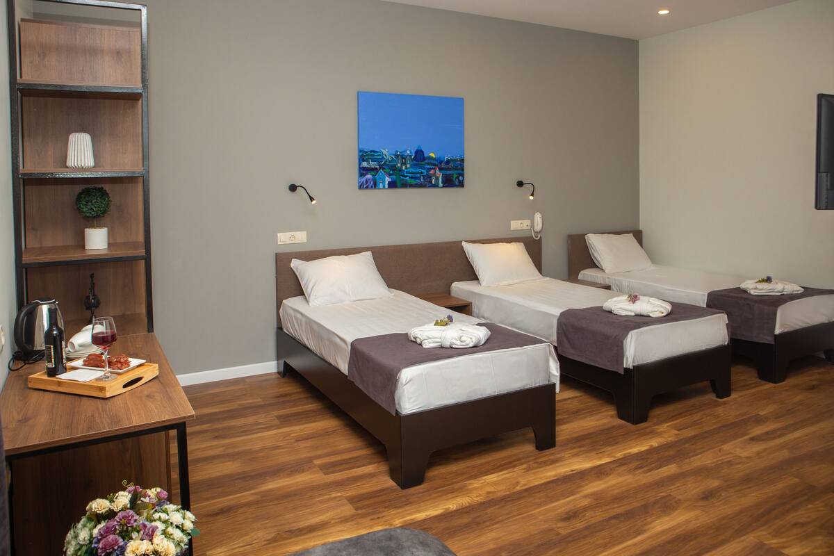 Habitación de hotel con tres camas, un escritorio de madera con una bandeja de comida y bebida, y un cuadro colgado en la pared.
