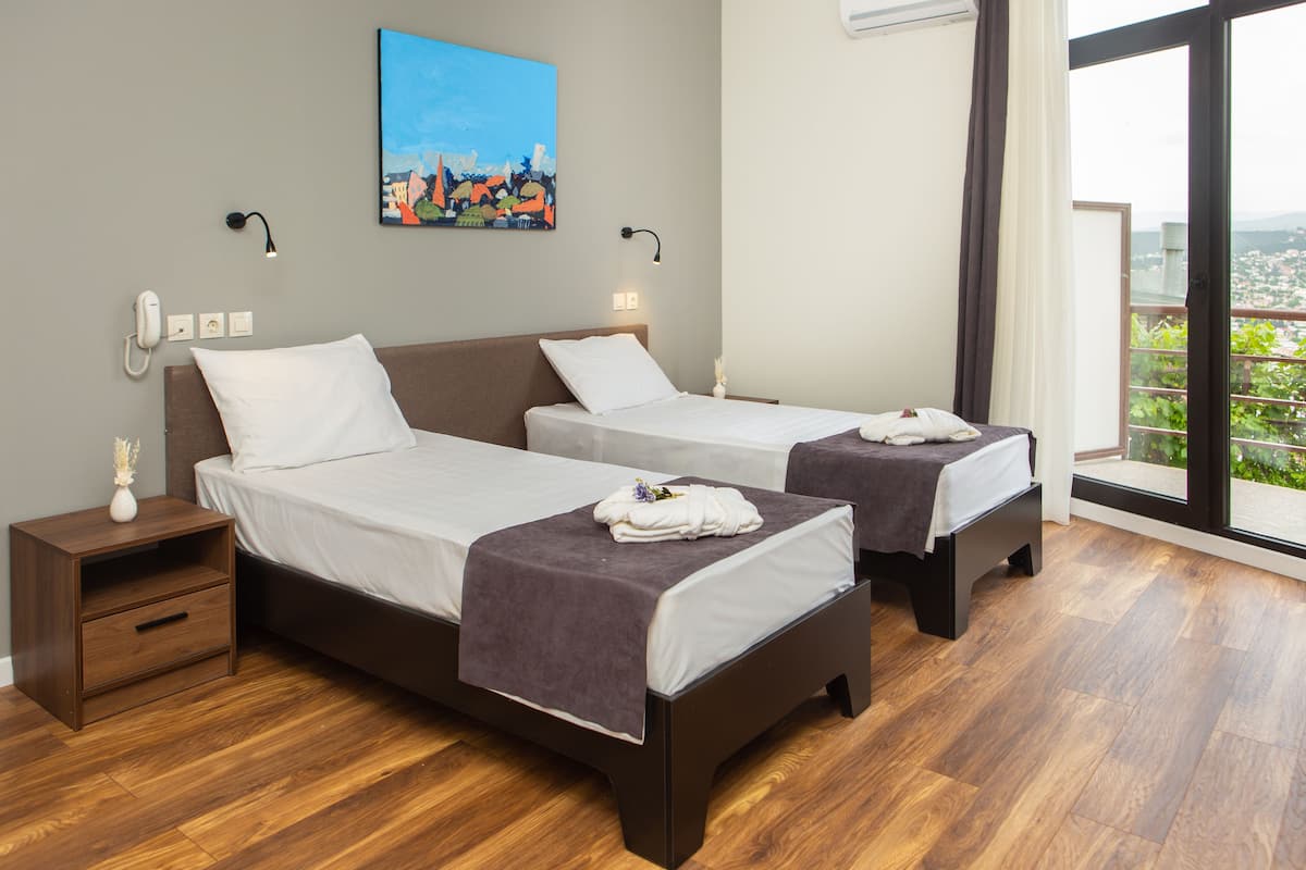Habitación de hotel con dos camas, una mesita de noche, un cuadro y vistas a la ciudad.