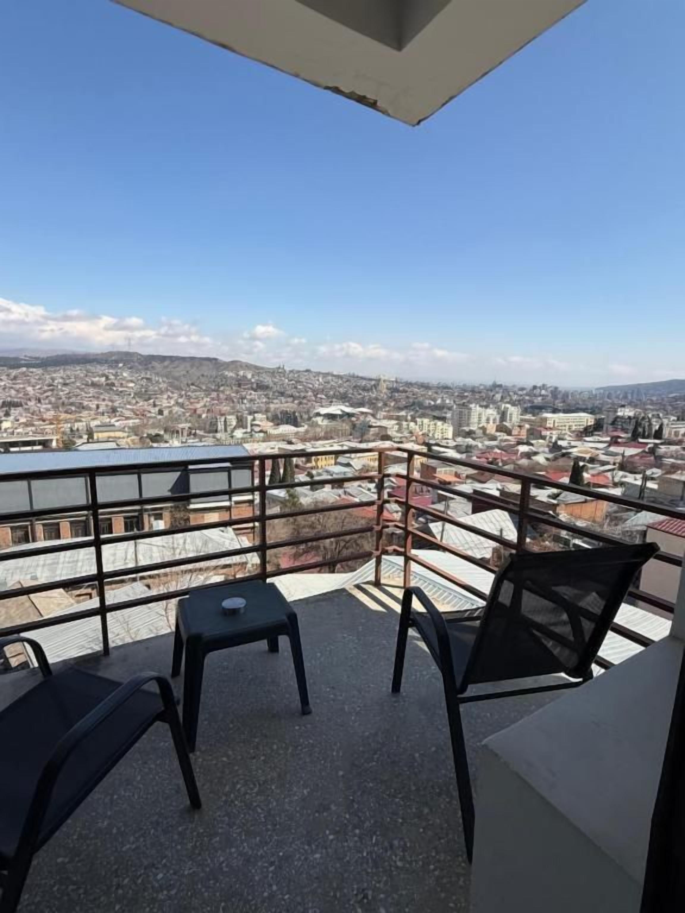 A balcony with a view of a cityscape, including buildings and a body of water.