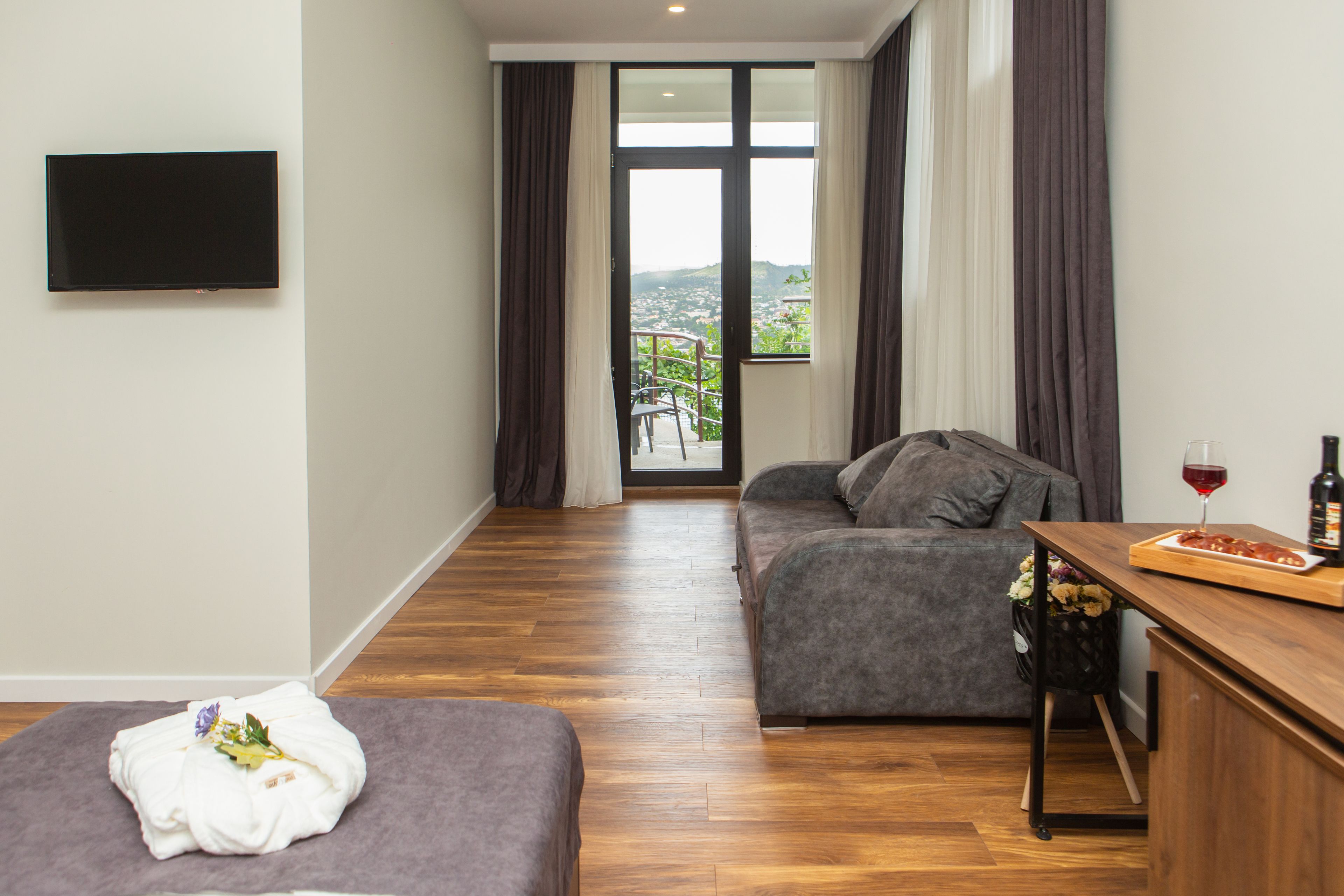 A modern living room with a sofa, a small table with a bottle of wine, and a view of a balcony with a railing.