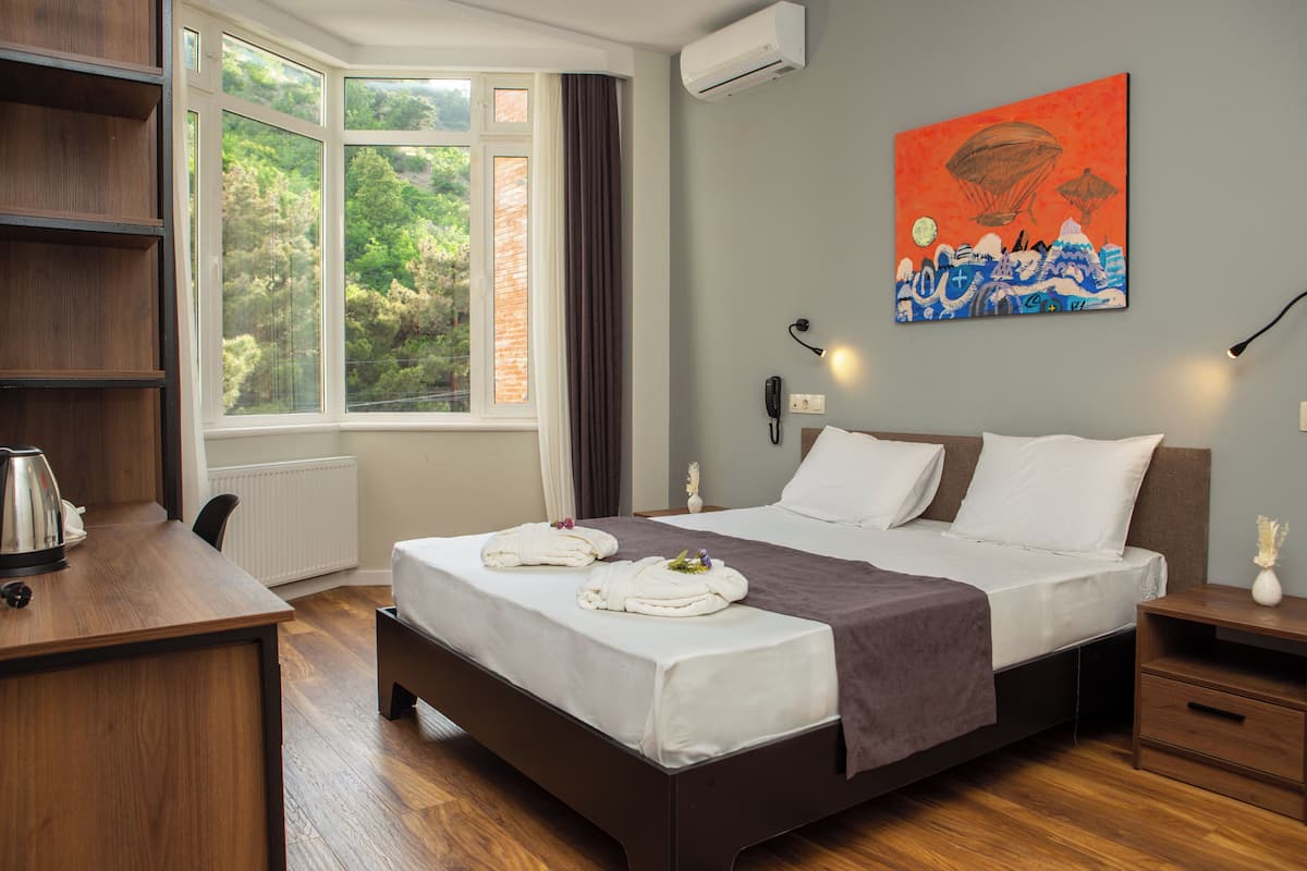 Una habitación de hotel con una cama grande, un escritorio con hervidor, una ventana con cortinas y un cuadro en la pared.