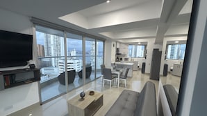A modern living room with a large TV, seating area, and a view of the city through floor-to-ceiling windows. - Luxury Stay in Cartagena Prime Beachfront + Views (Cartagena)
